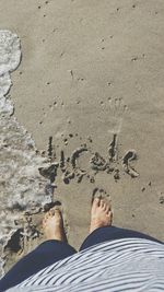 Low section of man standing in front of text on sandy beach