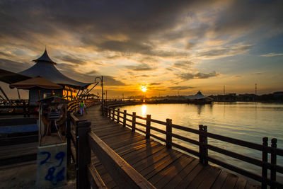 Pier over river against sky at sunset