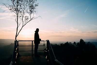 Silhouette man standing by railing against sky during sunset