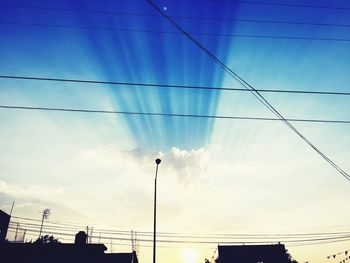 Low angle view of silhouette electricity pylon against blue sky