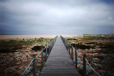 Boardwalk at sea shore against cloudy sky