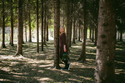 Portrait of woman standing by tree trunk in forest