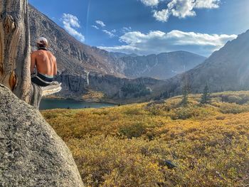 Rear view of person on rock by mountains against sky