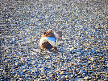 Side view of boy sitting on pebbles