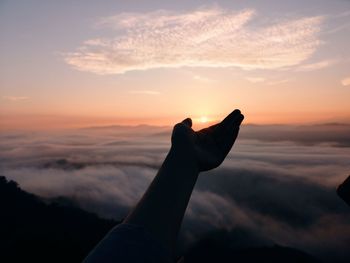 Optical illusion of silhouette hand holding sun against sky during sunset