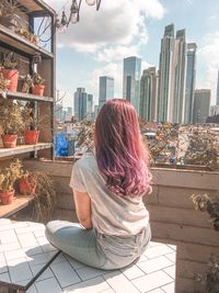 Rear view of woman sitting against buildings in city