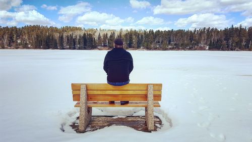 Rear view of man sitting on snow covered landscape