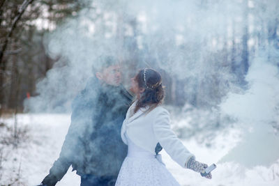 Close-up of couple with distress flare standing against tree during winter