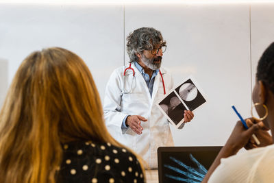 Elderly male medic explaining x ray image to unrecognizable coworkers while working in modern clinic