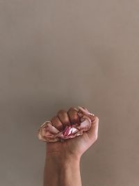 Cropped hand holding flower against wall