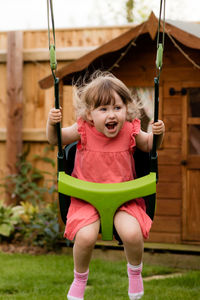 Happy girl screaming while swinging at backyard