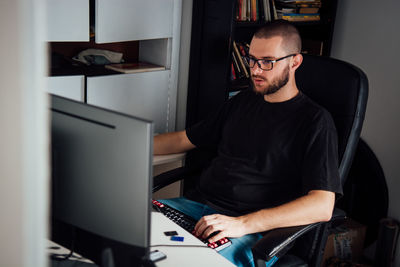 Side view of young man using computer while on chair at home