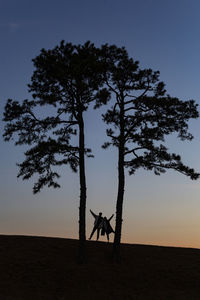 Silhouette of people with arms outstretched standing against sky against sunset