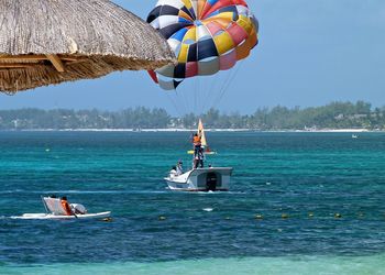 Man parasailing over boat and sea against sky on sunny day