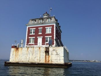 Lighthouse in sea against clear blue sky