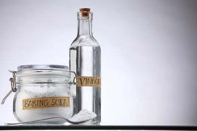 Close-up of baking soda and vinegar bottle against white background
