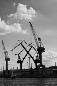 Cranes at commercial dock against cloudy sky