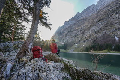 Rear view of hiker sitting on rock by river