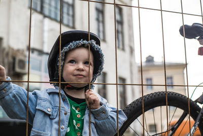Cute girl wearing cycling helmet while standing by fence