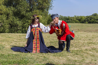 Portrait of man in traditional clothing kissing hand of woman while kneeling on field 