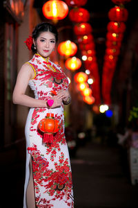Portrait of young woman wearing cheongsam while holding lantern during festival at night