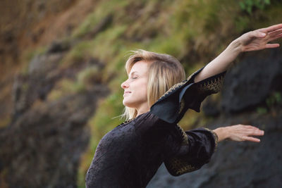 Side view of young woman with arms outstretched against rocky mountain