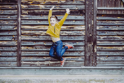 Full length of boy jumping against wooden wall