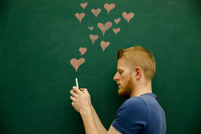 Young man using mobile phone with heart shapes on blackboard