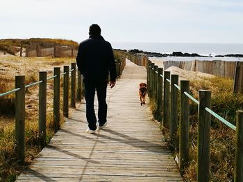 Rear view of man on boardwalk against sky