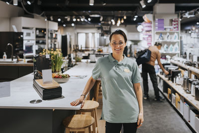 Portrait of confident saleswoman standing by table in appliances store