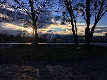 Bare trees on landscape against sky at sunset