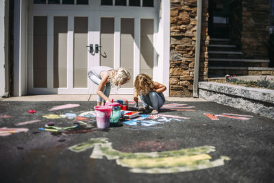Playful sisters painting on asphalt in front of house during sunny day
