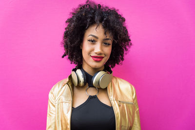 Fashionable young woman with curly hair against pink background