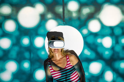 Unrecognizable young female in casual wear and vr headset getting new experience and touching virtual object in room with colorful projector illumination
