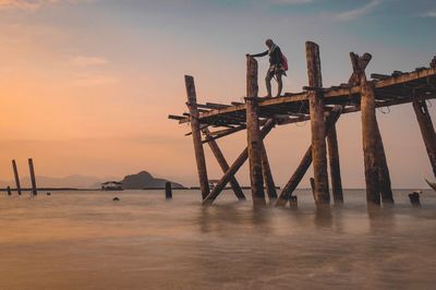 Low angle view of man standing on pier over sea against sky during sunset