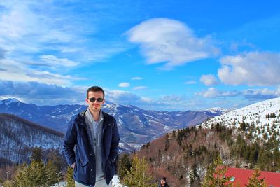 Portrait of man in sunglasses standing on snowcapped mountain