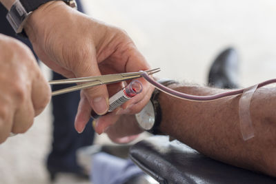 Cropped hands of doctor cutting iv drip tube connected to patient