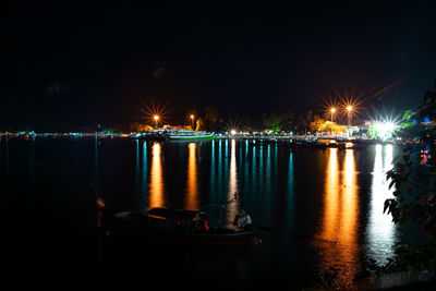 Illuminated city by river against sky at night