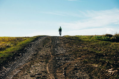 Rear view of woman riding bicycle on field against sky