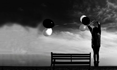 Child with balloons standing against cloudy sky