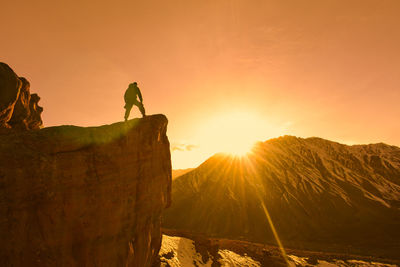 Low angle view of man standing on rock against sky during sunset