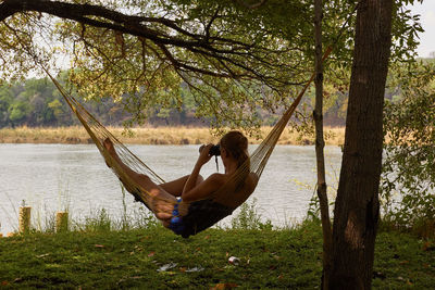 Woman relaxing in hammock looking through binoculars at lakeshore