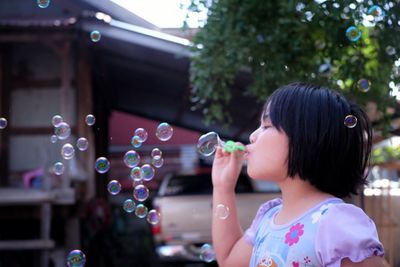 Girl blowing bubbles against trees