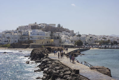 People on sea by buildings against clear sky