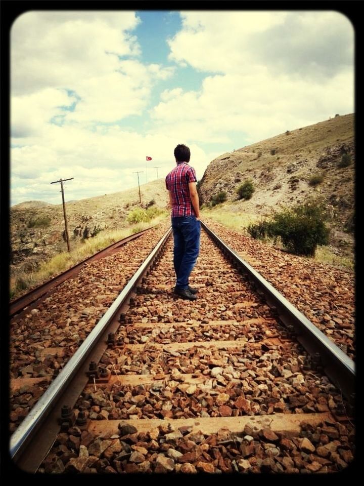 sky, full length, railroad track, lifestyles, rear view, leisure activity, cloud - sky, casual clothing, standing, the way forward, rail transportation, landscape, men, cloud, walking, diminishing perspective, nature, tranquility