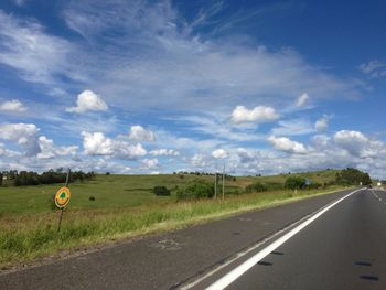 Road passing through field against cloudy sky