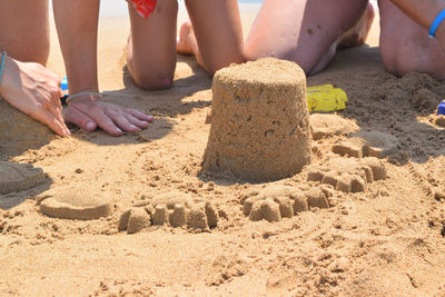 Low section of children by sandcastle at beach