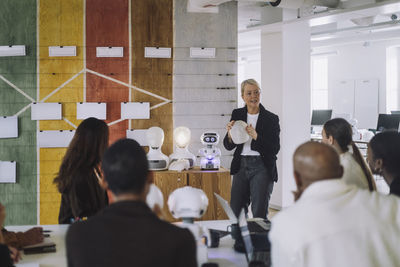 Mature teacher explaining multiracial students over robot in innovation lab