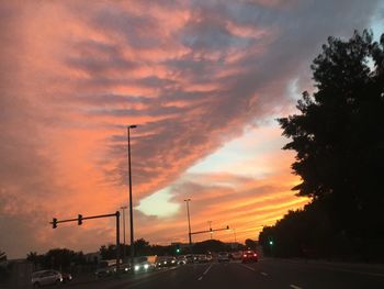 Cars on road against cloudy sky at sunset