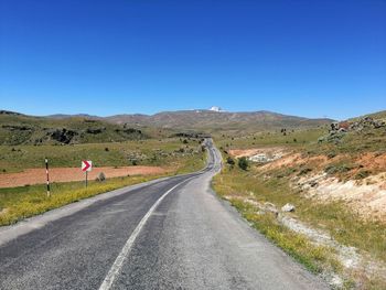 Road leading towards mountains against clear blue sky